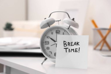 Ofisteki masasında kısa mesaj zamanı ve çalar saati olan kağıt, yakın plan.