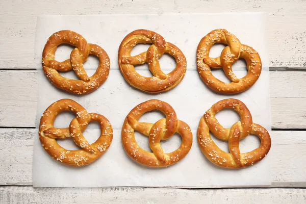 Beyaz ahşap arka planda lezzetli krakerler olan parşömen kağıdı, yakın plan.