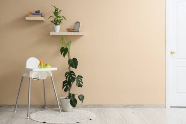 Bej duvarın yanında elma ve su şişesi olan bebek sandalyesi.