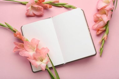 Açılmış boş defter ve pembe arka planda güzel gladiolus çiçekleriyle kompozisyon, yakın plan