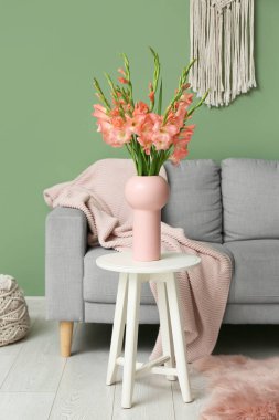 Oturma odasının iç tarafında bir buket güzel gladiolus çiçeği olan kanepe, masa ve vazo.