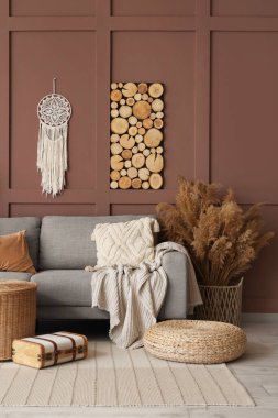 Rahat bir kanepe, hasır puf ve vazo. Oturma odasının içinde otlar var.