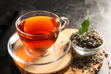 Ahşap tepsiyle kompozisyon, bir fincan siyah çay ve siyah grunge arka planda bir kase kuru yaprak, yakın plan.