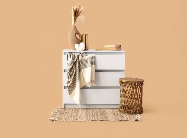 Hasır masa, çekmeceler ve vazoların modern sandığı bej arka planda otlar.