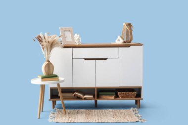 Mavi arka planda vazoları olan beyaz çekmece ve masa.