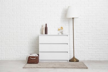 Beyaz tuğla duvarın yanında dekorlu ve lambalı çekmeceler.