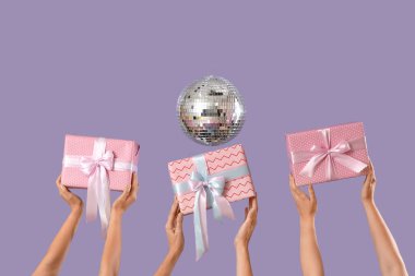 Hediye kutuları ve leylak arka planda disko topu olan kadın eller.