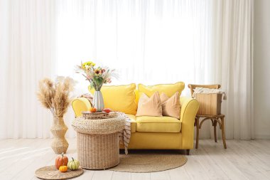 İçinde sarı kanepe ve vazoda sonbahar çiçekleri olan oturma odası.