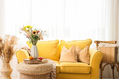 İçinde sarı kanepe ve vazoda sonbahar çiçekleri olan oturma odası.