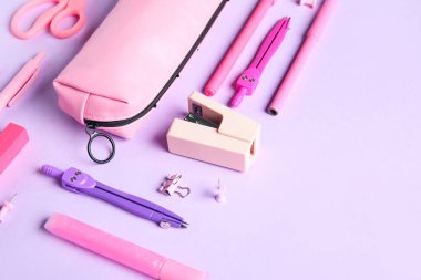 Leylak arka planında farklı kırtasiye malzemesi olan pembe kalem kutusu. Üst görünüm