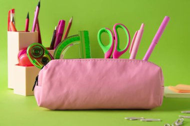 Yeşil zemin üzerinde farklı kırtasiye malzemesi olan pembe kalem kutusu