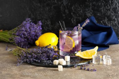 Bir bardak taze lavantalı limonata, çiçekler ve limonlar gri masada.