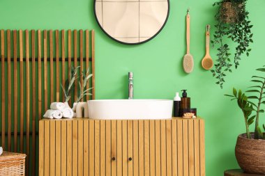 Lavabosu, çiçekleri ve yeşil duvarın yanındaki katlanabilir ekranı olan şık bir banyo.