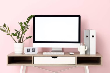 Ofiste modern bilgisayar, ev bitkisi ve saate sahip şık bir iş yeri var.