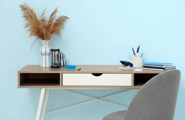 Rahat ofisteki mavi duvarın yanında vazo dolusu pampa, kırtasiye ve kum saati olan şık bir iş yeri.