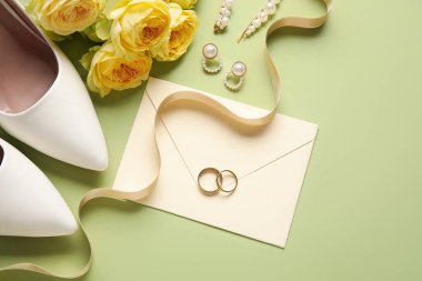 Zarflı alyanslar, kadın ayakkabıları, çiçekler ve yeşil arka planda mücevherler.