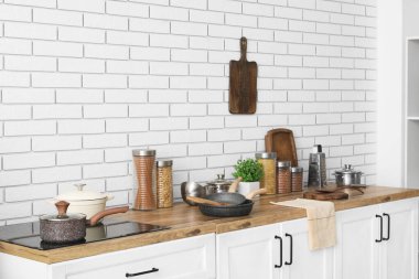 Mutfaktaki beyaz tuğla duvarın yanındaki masada makarna ve çatal bıçak dolu cam kavanozlar.