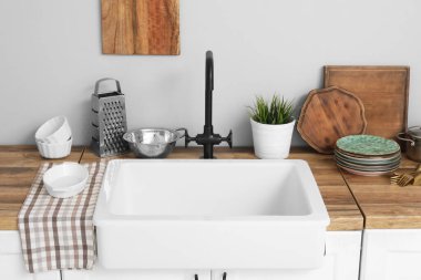 Ahşap tezgahta lavabo ve rahat mutfaktaki beyaz duvarın yanında tabaklar. Yakın çekim.