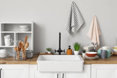 Seramik lavabo, temiz bulaşıklar ve ahşap mutfak tezgahındaki raf ünitesi.