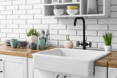 Mutfak tezgahında lavabo, temiz tabaklar ve hafif tuğla duvarın yanında bitkiler var.