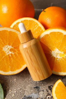 Bir şişe portakal yağı ve gri arka planda taze meyveler.