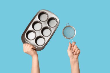 Mavi arka planda pişirme tenekesi olan elek tutan kadın.