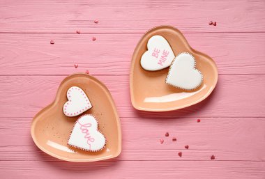 Kalp şeklinde kurabiyeler ve pembe ahşap arka planda dekor olan tabaklar. Sevgililer Günü kutlaması