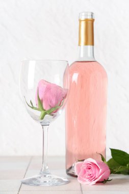 Bir şişe pembe şarap, cam ve beyaz fayans üzerinde güzel güller.