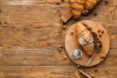 Çikolata kaplı tatlı kruvasan tahtaları ve ahşap arka planda fındıklar.