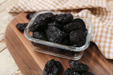 Beyaz ahşap arka planda kuru erikli cam kase, yakın plan.