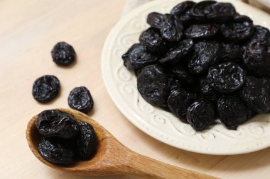 Bej ahşap arka planda kurutulmuş kuru erikli tabak ve kaşık.