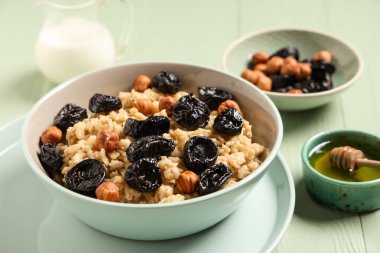 Bir kase lezzetli yulaf ezmesi, kuru erik, fındık ve bal yeşil ahşap arka planda.