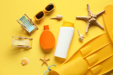 Paletlerle, güneş gözlükleriyle, deniz kabuklarıyla ve sarı arka planda güneş kremi şişeleriyle kompozisyon