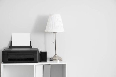 Modern yazıcı ve lambalı şık raf ünitesi beyaz duvarın yanında, yakın plan.