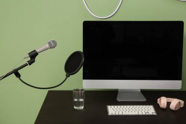 Kayıt stüdyosundaki yeşil duvarın yanında boş bilgisayar monitörü ve mikrofonu olan işyeri