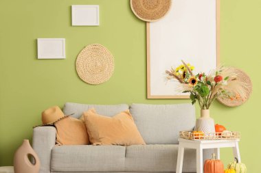 İçinde kanepe, boş çerçeveler ve vazoda sonbahar çiçekleri olan oturma odası.