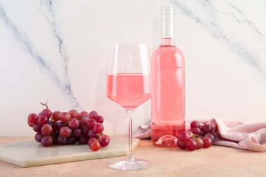Bardak ve bir şişe lezzetli pembe şarap ve bej masada taze üzümler.