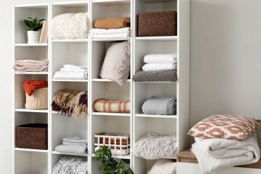 Beyaz duvarın yanında temiz çarşaf ve ekose kumaşlı raf ünitesi.