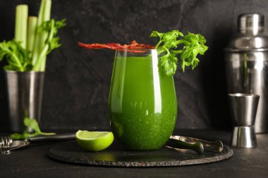 Bir bardak yeşil Bloody Mary kokteyli, domuz pastırması, kereviz ve siyah arka planda limon.