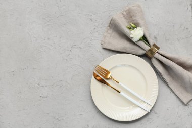 Altın çatal bıçak takımı ve gri arka planda östoma çiçekleri olan güzel bir masa.