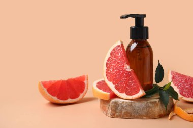 Bir şişe kozmetik ürünü, bej arka planda greyfurt ve taş parçaları, yakın plan.