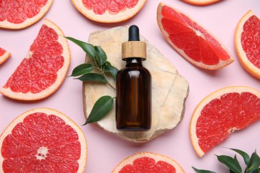 Bir şişe kozmetik ürünü, pembe arka planda greyfurt ve taş dilimleri, yakın plan.