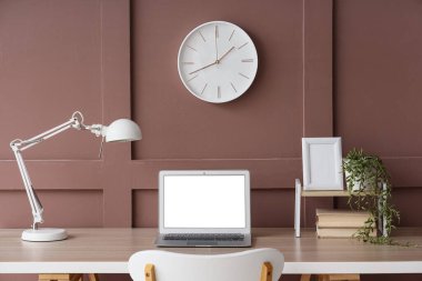 Ofisteki kahverengi duvarda boş dizüstü bilgisayarı ve saati olan işyeri