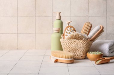 Kozmetik ürünleri şişeleri, hasır sepet ve bej fayans arka planda farklı masaj vücut fırçaları, yakın çekim