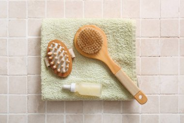 Temiz havluyla kompozisyon, bir şişe kozmetik ürün ve bej fayanslı vücut fırçaları, yakın plan.