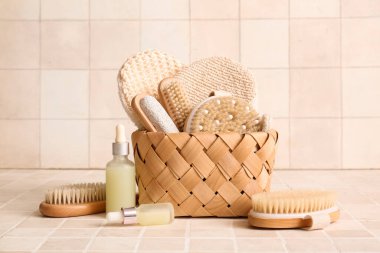 Hasır sepetli kompozisyon, kozmetik ürünleri şişeleri ve bej kaplamalı farklı masaj vücut fırçaları, yakın plan.