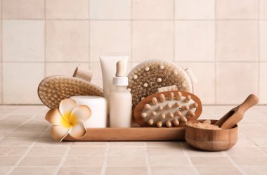 Ahşap tepsi, farklı masaj vücut fırçaları, şişeler ve bej kaplamalı kozmetik ürünler kavanozu, yakın plan.