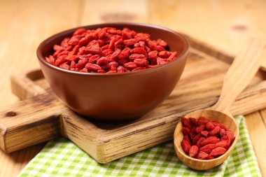 Tahta kesme tahtası, kase ve kaşıkla ahşap arka planda kurutulmuş kurt üzümü, yakın plan.