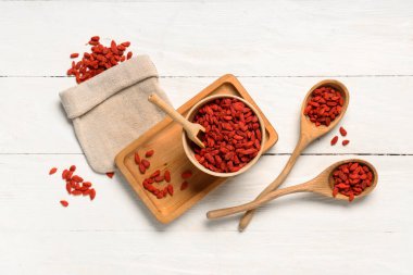 Tepsi, çanta, kase ve beyaz ahşap arka planda kurutulmuş goji üzümleri ile kompozisyon