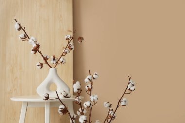 Oturma odasındaki bej duvarın yanındaki masada pamuk çiçekli vazolar, yakın plan.